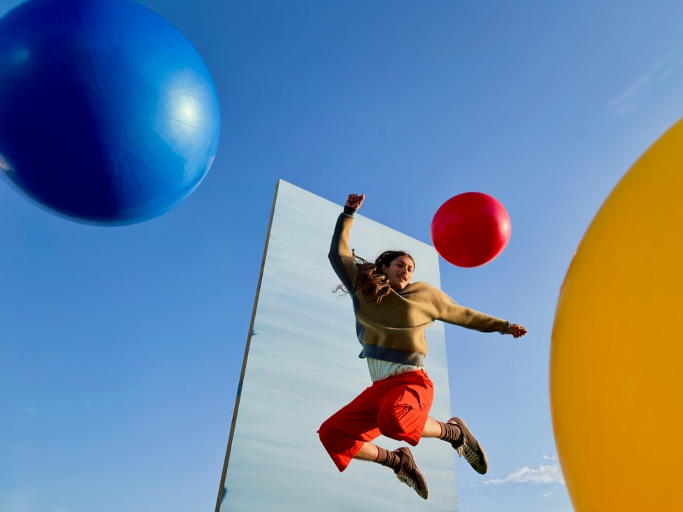 En person hopper foran en speilflate mellom store blå, røde og gule baller under en klar himmel.